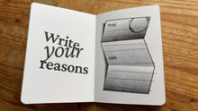 Load image into Gallery viewer, An open notebook or journal lying on a wooden surface, showing a white cover with the phrase 'Write your reasons' in large black text and a black-and-white illustration of an open book on the inside page.
